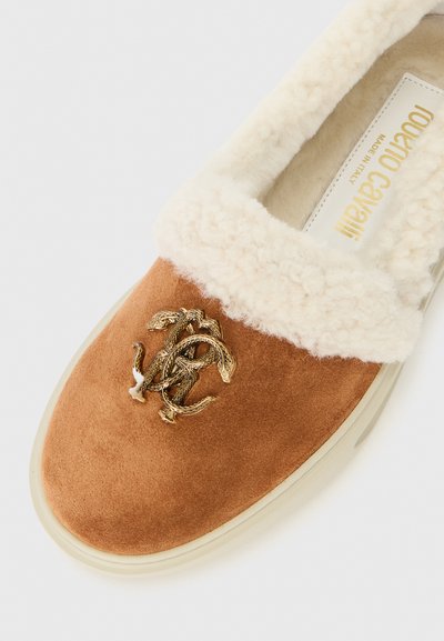 Brown suede slip-on shoe with white fluffy lining, featuring a golden snake and logo detail on the upper. Clear rubber sole.
