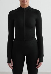 Haut noir à manches longues avec col montant, zip frontal intégral et coupe ajustée, fabriqué en tissu lisse et extensible.