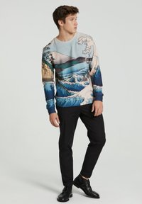 Pikendatud varrukatega särk, millel on sinise ja beeži lainekujundus koos mägise aktsentidega, valmistatud pehmest kangast. Kombineeritud mustade pükste ja kingadega.