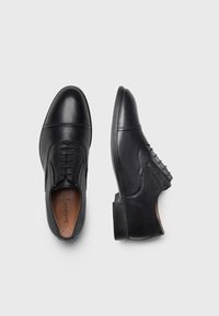 Bottines en cuir noir avec des surfaces lisses et texturées, présentant un design à lacets sur l'une et une couture détaillée sur l'autre.
