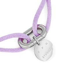 Collana con corda intrecciata viola, chiusura in metallo argento a gancio e una targhetta rotonda incisa con "C P H STUDIOS." Presenta una texture liscia e lucida.