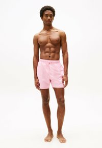 Pantaloni da bagno rosa con vita elastica e cordoncino, texture liscia, taglio fino al ginocchio e senza motivi o dettagli visibili.