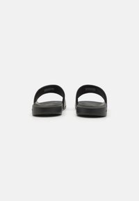 Des tongs noires au design minimaliste, avec une semelle en caoutchouc lisse et deux larges sangles pour le soutien et le confort.