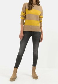 Beige sweater med gule og grå striber; ribbede manchetter og kant. Kombineret med mørke skinny jeans og sandfarvede ruskinds ankelstøvler.