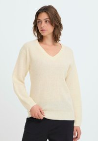 Cremfarbener Strickpullover mit V-Ausschnitt, langen Ärmeln und gerippten Bündchen, mit einer strukturierten Stoffqualität und lässiger Passform.