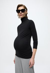 Μαύρο μακρυμάνικο τοπ με λαιμόκοψη ζιβάγκο, με ρυτιδωτές πλευρές, σε συνδυασμό με γκρι φούστα. Το ύφασμα φαίνεται απαλό και ελαστικό.