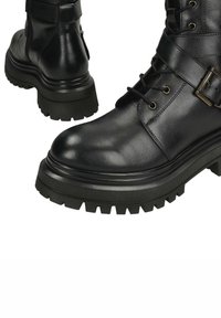 Černé kožené bojové boty s robustní gumovou podrážkou, šněrováním, kovovými doplňky a texturovaným povrchem pro lepší přilnavost.