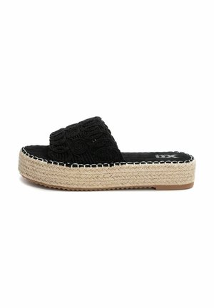 Sandalia de tiras negra con parte superior texturizada que presenta patrones circulares, suela de plataforma de yute y detalles de costura a lo largo del borde.