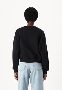 Sudadera negra con un corte relajado, hombros caídos y ribetes en el dobladillo. Combinada con jeans de cintura alta de color azul claro.