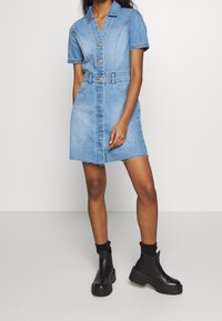 Sukienka dżinsowa z krótkimi rękawami, niebieski l delikatnym zniszczeniem, zapięcie na guziki z przodu, marszczona talia, postrzępiony dół, w połączeniu z czarnymi botkami za kostkę i czarnymi skarpetkami.