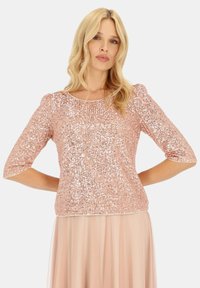 Top z cekinami w kolorze różowego złota, z rękawami do trzech czwarte, okrągłym dekoltem i dopasowanym krojem, charakteryzujący się gładką, błyszczącą fakturą.