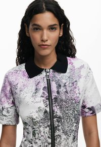 Robe zippée à manches courtes en blanc avec un motif abstrait texturé en violet et noir, dotée d'un col noir et d'une fermeture éclair à l'avant.