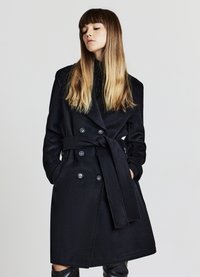 Cappotto trench nero doppiopetto con cintura, caratterizzato da grandi bottoni e tasche laterali. Tessuto morbido con una texture liscia.