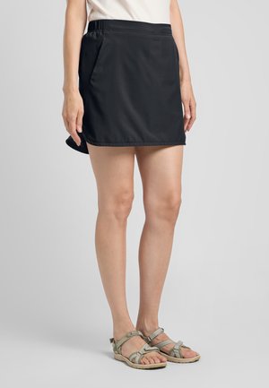 Zwarte sportrok met een elastische tailleband en zijzakken. Draagt lichte grijze sandalen met verstelbare banden.
