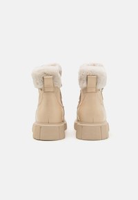 Botas de tobillo beige con un suave cuello de piel, cuero texturizado y suela de plataforma resistente. Cuenta con un tirador en el talón para ponerlas fácilmente.