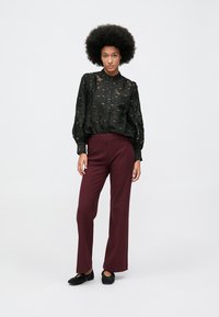 Čierna priehľadná blúzka s textúrovaným vzorom, voľný strih, zapínanie na gombíky, skombinovaná s červenohnedými nohavicami s vysokým pásom a čiernymi sieťovinovými espadrilkami.