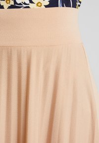 Gonna di tessuto testurizzato color pesca con vita alta e pieghe fluide. Il design presenta un materiale leggero e liscio.