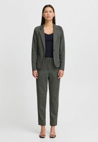 Costume sur mesure en motif pied-de-poule noir et blanc, composé d'un blazer et d'un pantalon slim. Porté sur un top noir. Tissu lisse.