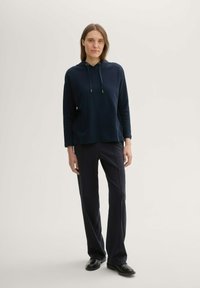 Felpa navy con superficie testurizzata, chiusura con cordoncino e tasca frontale, abbinata a pantaloni scuri abbinati e scarpe nere.