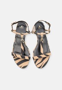 Sandaler med remmer i svart og beige zebra mønster, med glatt lær og en gylden ananasdetalj på tåremmen.