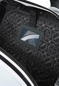 Interior de mochila con forro negro estampado con diseños florales. Incluye una ventana transparente para identificación y un bolsillo elástico para almacenamiento.