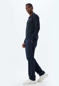 Dunkelblaues Langarm-Polo und passende Hose, aus weichem Stoff, mit lockerer Passform. Weiße Sneaker runden das Outfit ab.