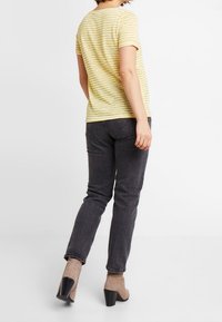 Geel en wit gestreept t-shirt, met korte mouwen, gecombineerd met zwarte jeans en beige enkellaarsjes met hak, gezien vanuit de rug.