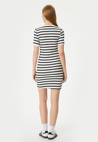 Zwart-wit gestreepte bodycon jurk met korte mouwen, ronde hals en een aansluitende silhouet. Gecombineerd met witte sokken en zwarte schoenen.