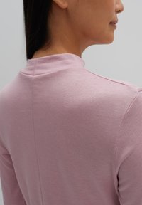 Helles rosa Oberteil mit langen Ärmeln und Stehkragen, glatter Textur und Nahtdetails an der Rückseite, das eine figurbetonte Silhouette zur Schau stellt.