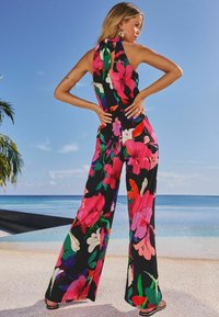 Juodi jumpsuit'ai su spalvingais rožiniais ir žaliais gėlių raštais. Apima raištį nugaroje ir plačią kojas, užtikrinančius laisvą prigludimą.
