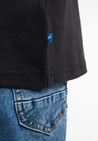 Sort bomulds t-shirt med et lille blåt mærke på sømmen, parret med lyseblå denim jeans med en synlig lomme og syningsdetalje.