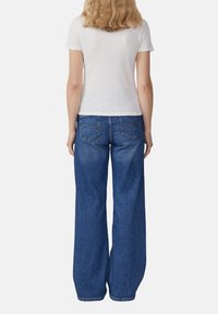 Witte geribde top met korte mouwen, gecombineerd met hooggeritste blauwe jeans met wijde pijpen, voorzien van twee achterzakken en contrasterende stiksels.