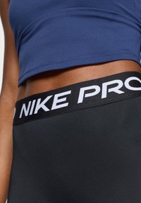 Μαύρα αθλητικά κολάν με φαρδύ μαύρο λάστιχο που έχει λευκή επωνυμία "NIKE PRO", συνδυασμένα με ένα εφαρμοστό σκούρο μπλέ μπλουζάκι cropped.