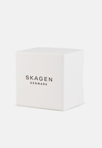 Scatola quadrata bianca con il testo "SKAGEN" e "DENMARK" in carattere nero sul davanti, con bordi puliti e superficie liscia.