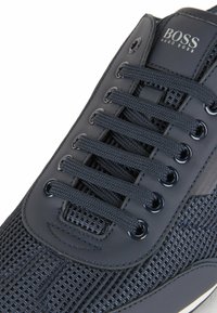 Marinblå sneakers med överdel i mesh, gummibeklädnad, runda skosnören och metallöglor, med en diskret logotyp på tungan.