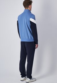 Pullino blu e blu navy con colletto alto, con accenti bianchi sulle maniche. Abbinato a pantaloni navy e sneakers bianche.