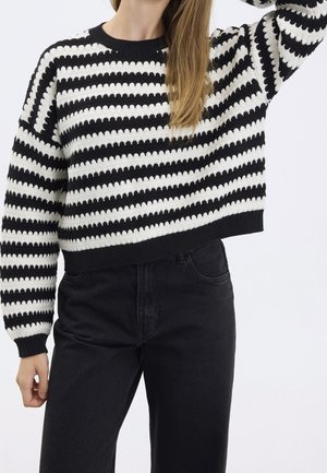 Schwarz-weiß gestreifter Strickpullover mit einem gerippten Rundhalsausschnitt und -bündchen. Weite, cropped Passform. Kombiniert mit hochgeschnittenen schwarzen Jeans.