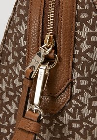 Brązowa torebka z teksturowanej skóry, złotym okuciem i beżowym materiałem w wzory. Posiada wyraźny zamek błyskawiczny i odczepiany pasek.