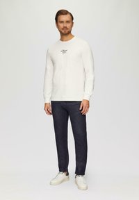 T-shirt en coton blanc à manches longues avec le logo "s.Oliver", associé à un jean en denim foncé et des baskets blanches pour un look décontracté.