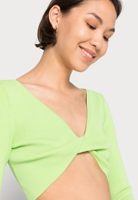 Top cropped de malha canelada verde-lima com decote em V profundo e detalhe torcido na parte da frente, apresentando mangas longas e um corte ajustado.