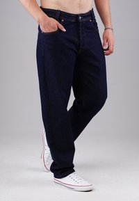 Dunkelblaue Jeans im Straight-Leg-Stil, mit sichtbaren Nähten, Taschen und einem Knopfverschluss, kombiniert mit weißen Sneakern.