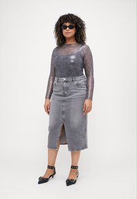Top trasparente a maniche lunghe con motivo leopardato, gonna midi in denim grigio con spacco frontale e décolleté nere a punta con cinturini.