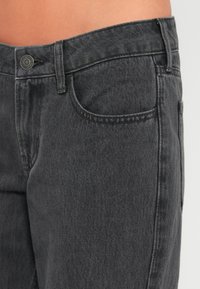 Μαύρα τζιν από denim με κλασικό σχέδιο, πέντε τσέπες και διακριτική ξεθωριασμένη υφή, με κούμπωμα από μεταλλικό κουμπί.