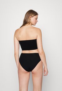 Μαύρο δίχρωμο μπικίνι με στράπλες τοπ και ψηλόμεσο κάτω μέρος, κατασκευασμένο από απαλό ύφασμα με ελάχιστες ραφές και χωρίς διακοσμητικά στοιχεία.