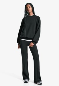 Sort sweatshirt med rund hals og dropped shoulders, parret med sorte flared bukser med sidefuger. Modellen har sportssko på.