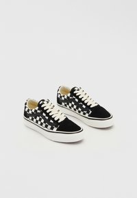 Zapatillas con un patrón de tablero de ajedrez en blanco y negro, hechas de materiales de ante y lona, con cordones blancos y una suela de goma.