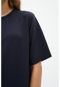 Granatowa koszulka z krótkim rękawem, wykonana z miękkiego materiału, z klasycznym okrągłym dekoltem i gładką fakturą, z prostymi detalami przeszycia.