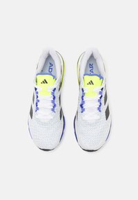 White athletic shoes with a textured mesh upper, black accents, bright yellow and blue detailing, and white laces. Rounded toe design.