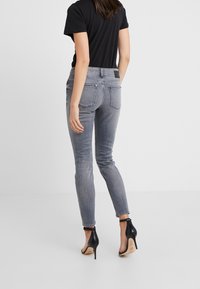 Pantalones ajustados gris claro con un lavado desgastado, bolsillos traseros y una etiqueta negra en la cintura. Combinados con zapatos de tacón negro.