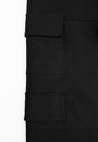 Zwarte stof met een getextureerd diagonaal patroon, met meerdere rechthoekige zakken van verschillende groottes die verticaal zijn gerangschikt.